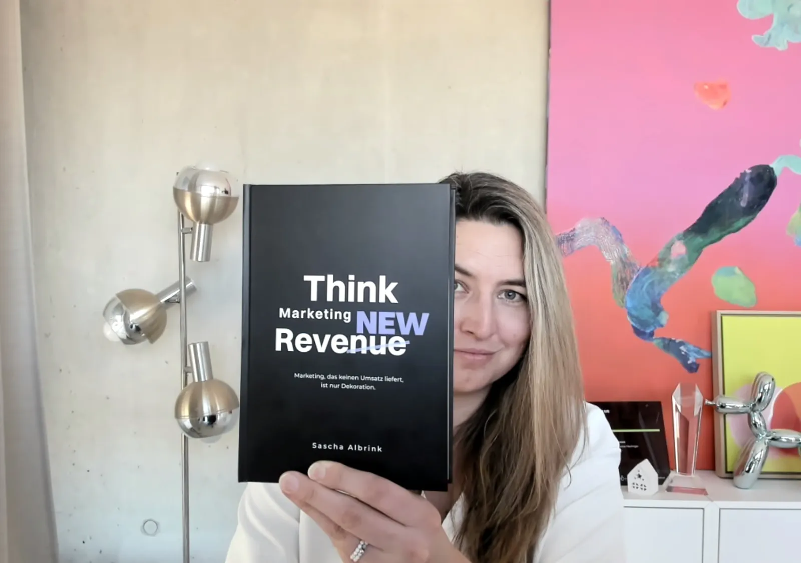 Eine Frau hält in einem modernen Raum ein schwarzes Buch mit dem Titel „Think Marketing NEW Revenue“ von Sascha Albrink in der Hand.