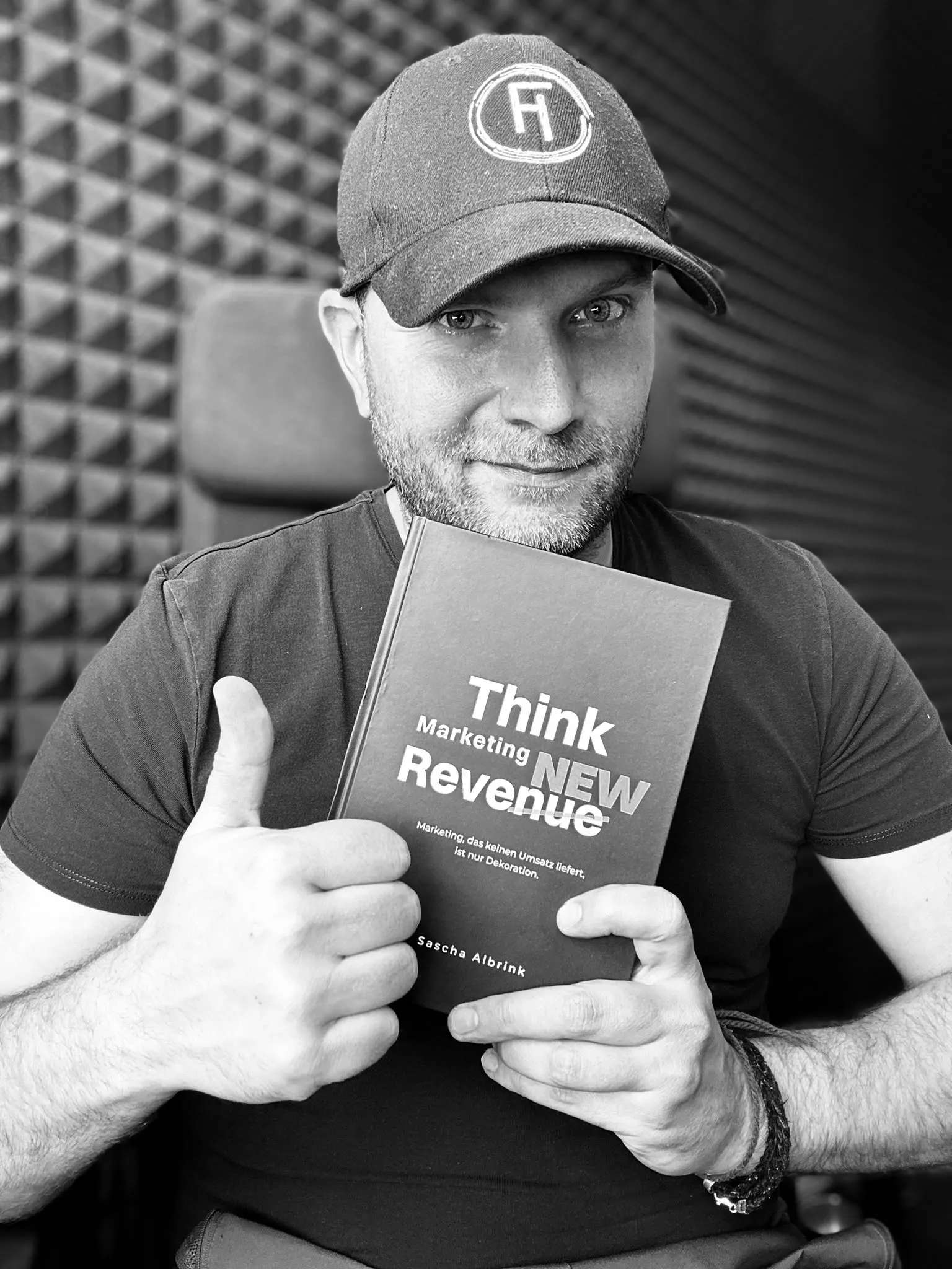 Ein Mann mit einer Cap hält ein Buch mit dem Titel „Think Marketing New Revenue“ in der Hand und zeigt den Daumen nach oben.