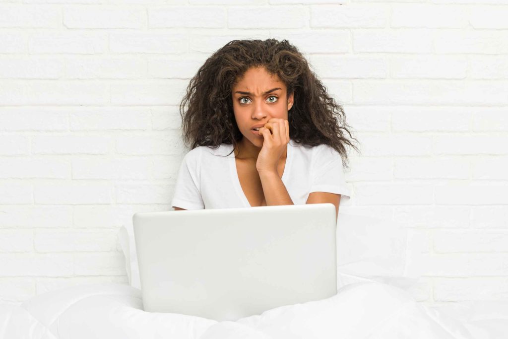 woman-sitting-bed-with-laptop-biting-fingernails