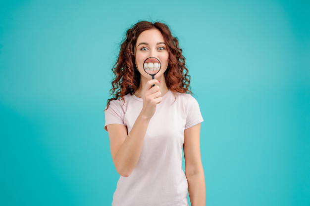 attractive-woman-with-curly-hair-showing-teeth-through-magnifying-glass-teeth-cleaning-dental-blog