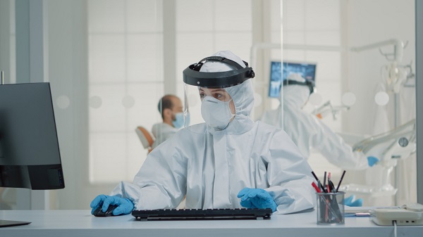 dentist-assistant-sitting-desk-using-computer-during-third-wave-using-ppe-kit