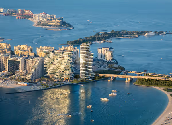 Vue aérienne d'un complexe résidentiel moderne sur la côte avec plusieurs yachts dans l'eau bleue et une longue jetée.