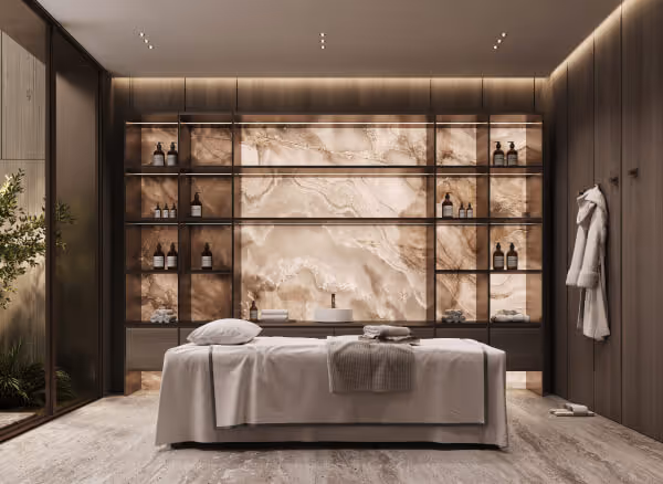 Salle de massage moderne avec une table de soin couverte de draps blancs, murs en bois sombre, étagères avec des bouteilles et une grande paroi en marbre beige.