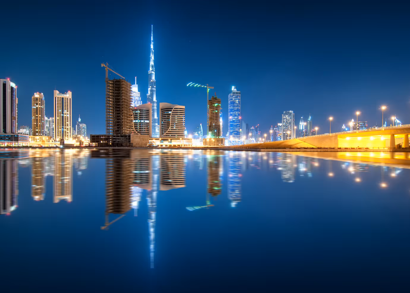 Paysage urbain nocturne de Dubaï avec le Burj Khalifa illuminé se reflétant dans l'eau calme.