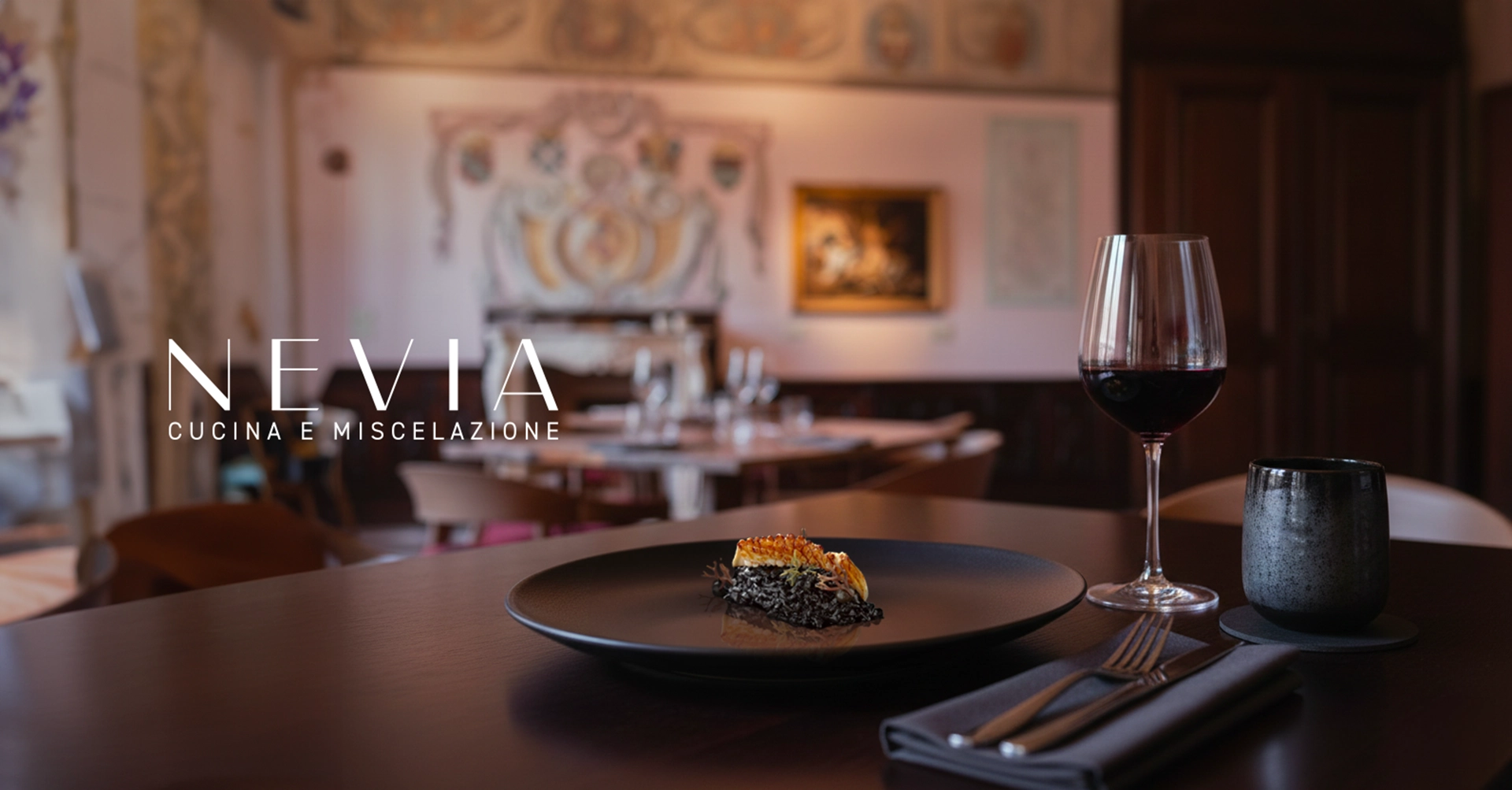 Piatto gourmet e calice di vino sul tavolo del ristorante Nevia – Cucina e Miscelazione a Villarbasse (Torino), con la sala sullo sfondo, fotografia d’atmosfera realizzata da Digistart.