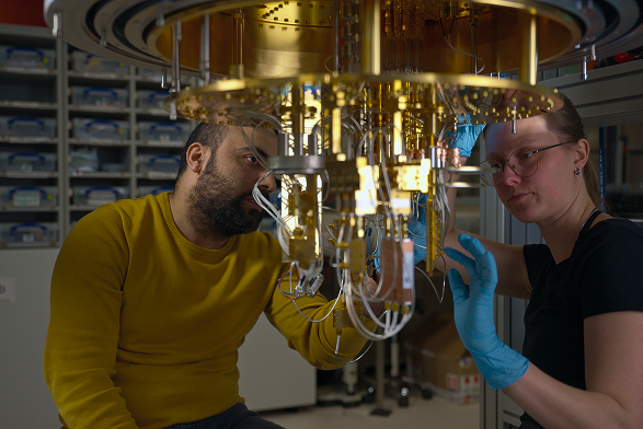 Two scientists, a man and a woman wearing blue gloves, working closely with a complex scientific apparatus in a laboratory.