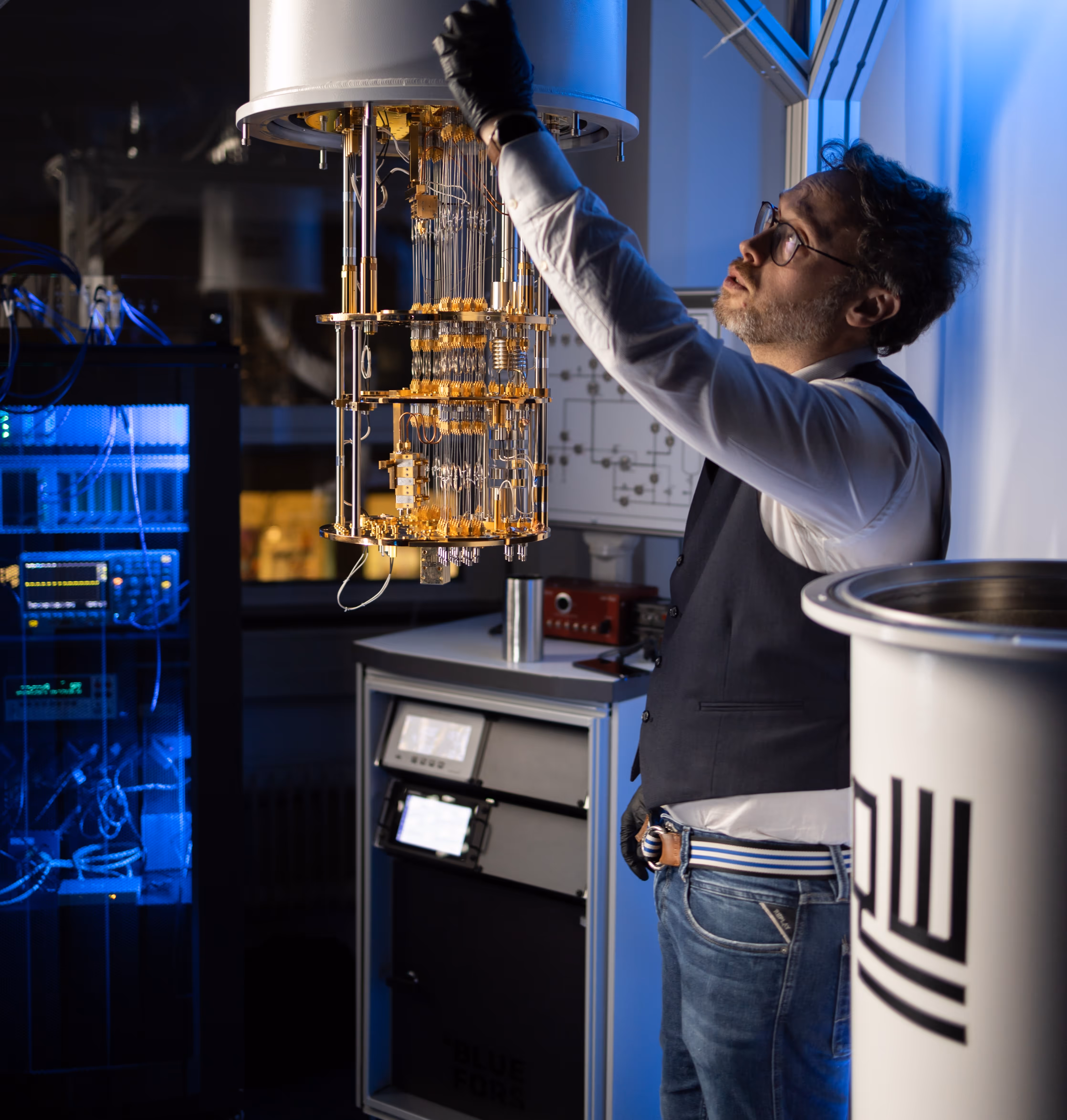 Scientist wearing glasses and black gloves adjusting a quantum computer in a lab with blue lighting.
