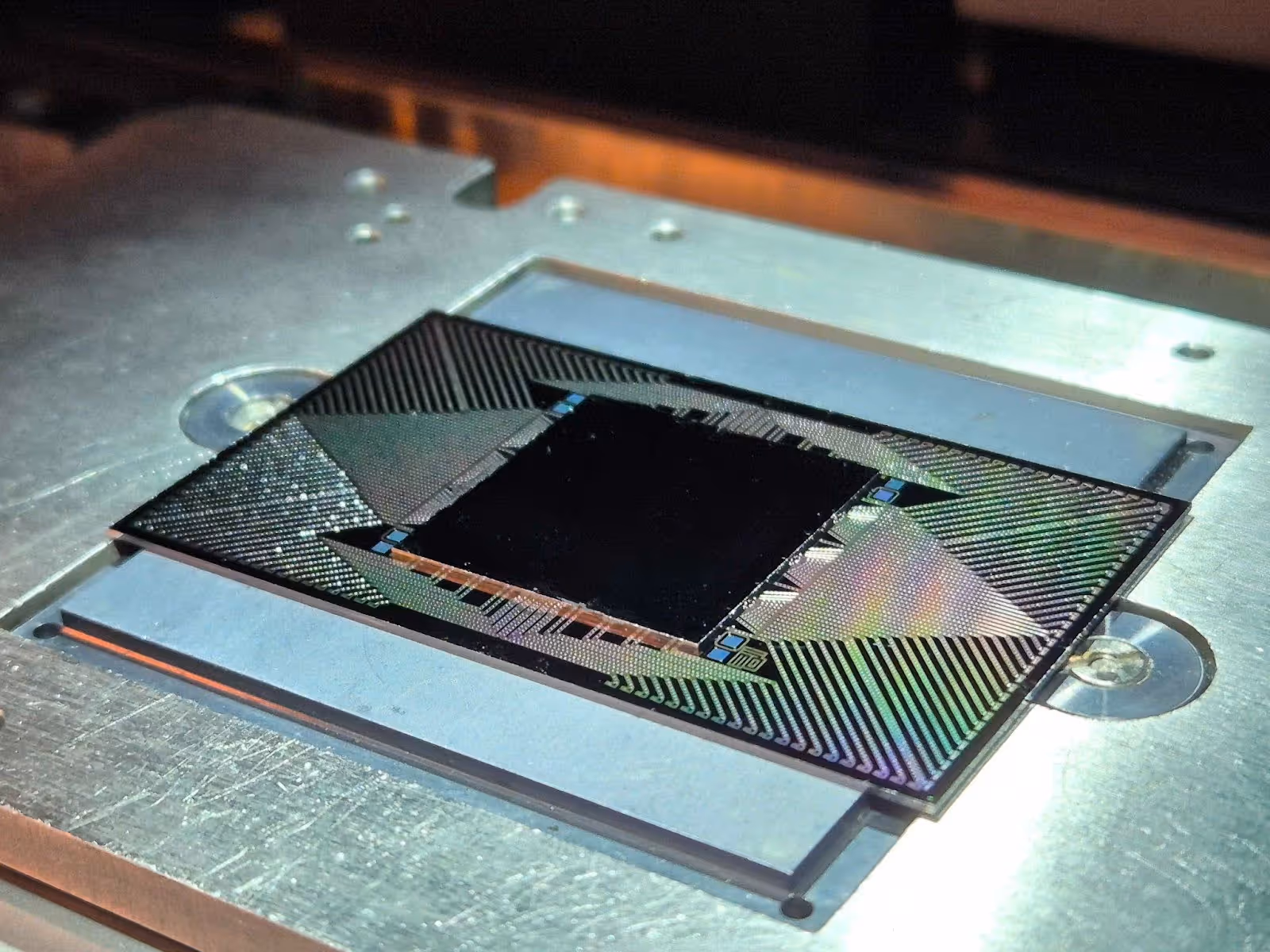 Close-up of QuantWare’s superconducting quantum processor chip, Tenor, mounted on a metallic platform, showing intricate wiring patterns and reflective surfaces.