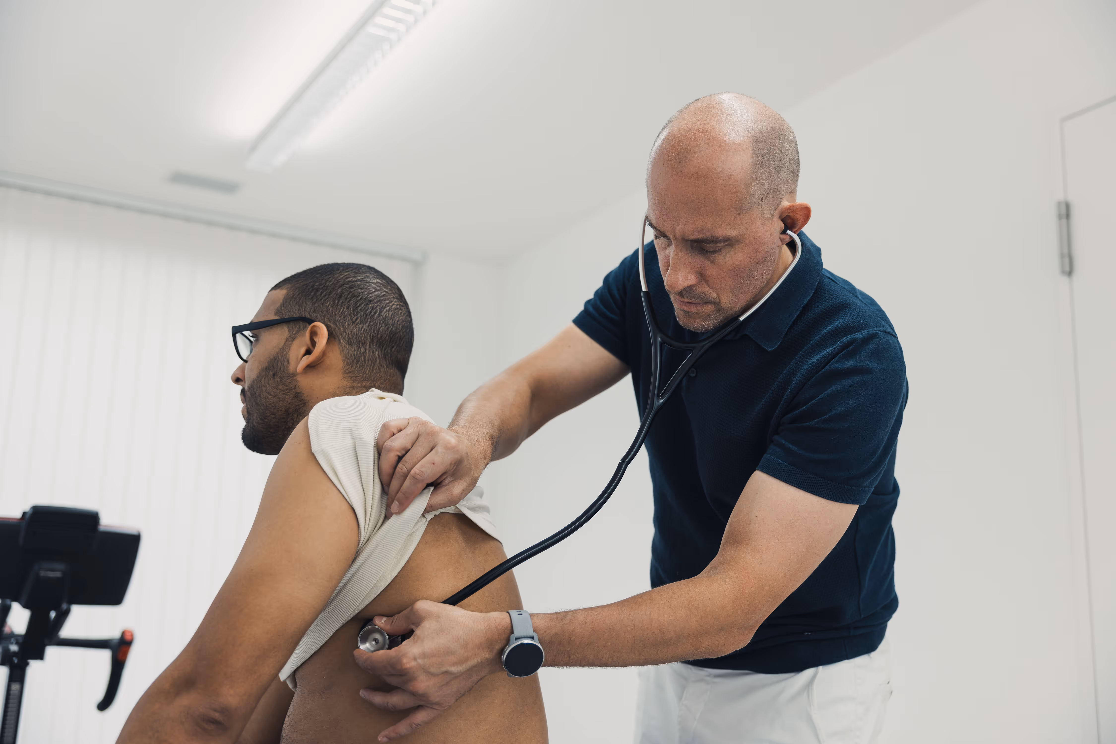 Doctor using a stethoscope to listen to a patient's back in a clinical setting.