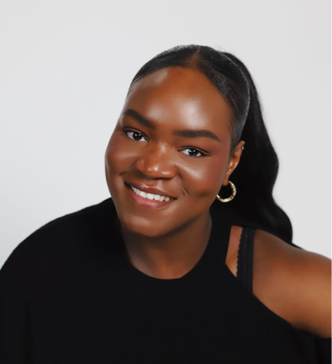 Smiling woman with dark skin, long black hair tied back, wearing gold hoop earrings and a black top.