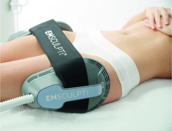 Person lying on back undergoing EMSCULPT body contouring treatment on abdomen with device strapped around waist.