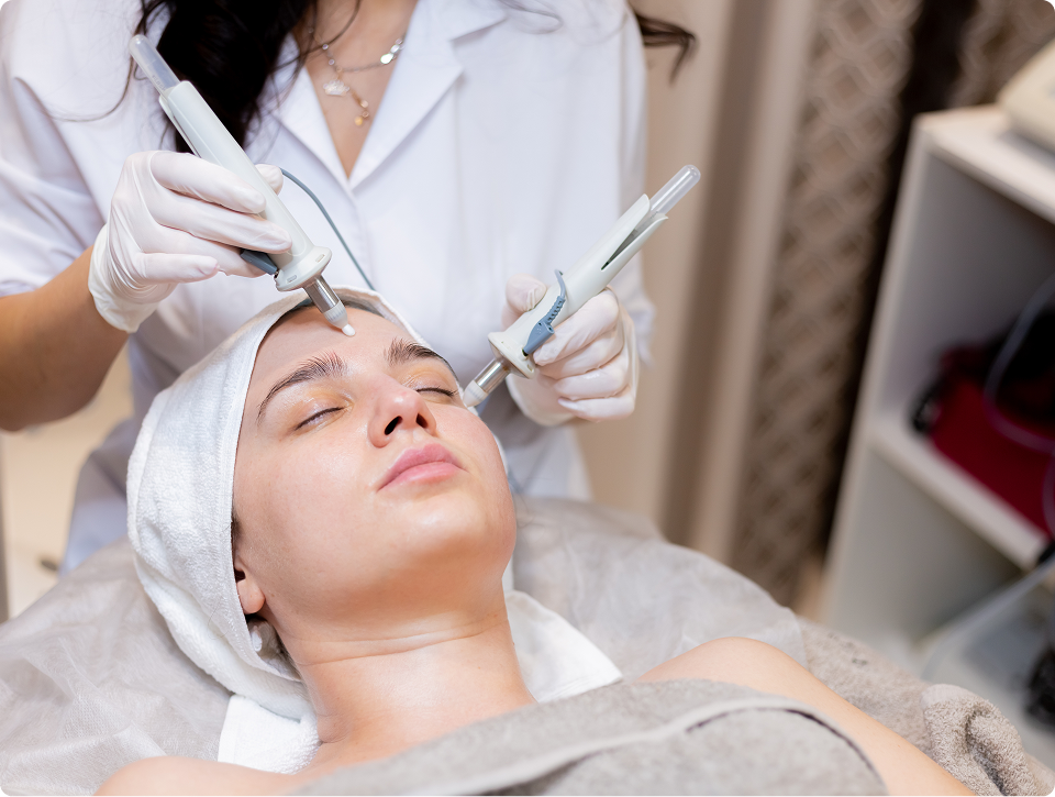 Woman receiving a dual handpiece facial treatment from a skincare professional wearing gloves and a white coat.