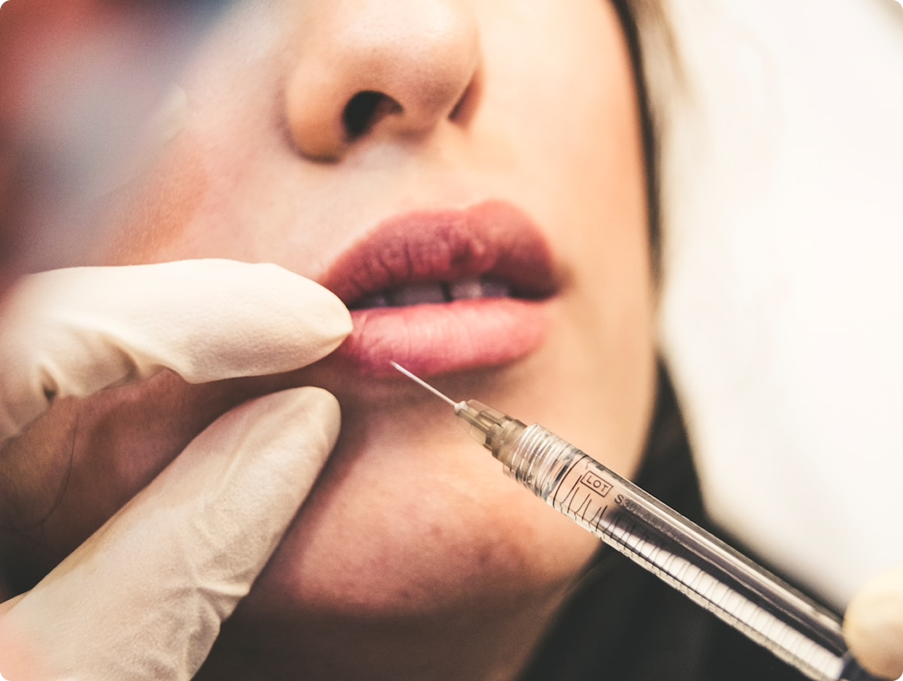 Close-up of a person's lips about to receive an injection from a syringe held by a gloved hand.