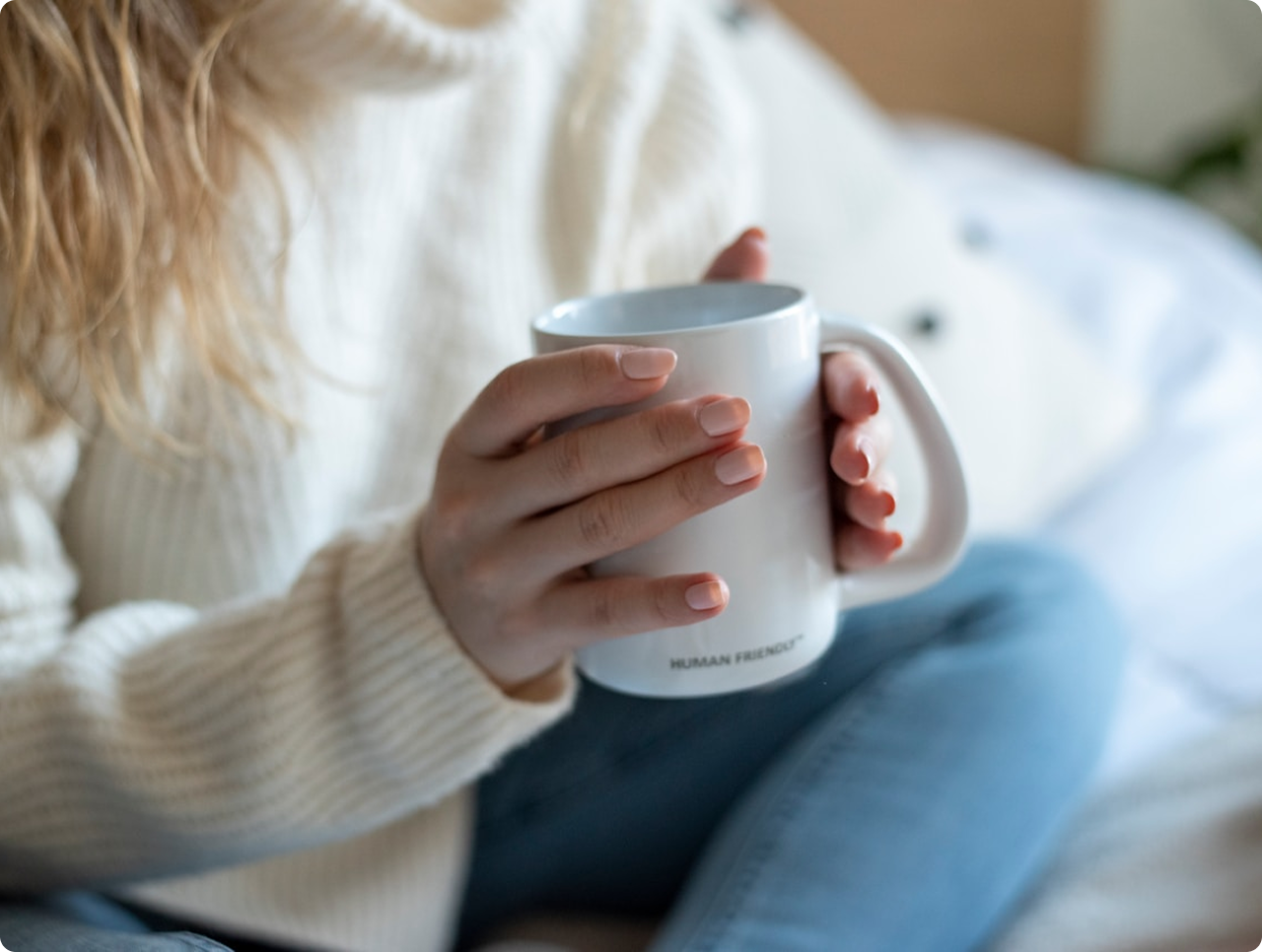 Person wearing a cream sweater holding a white mug with the words 'HUMAN FRIENDLY' on it.