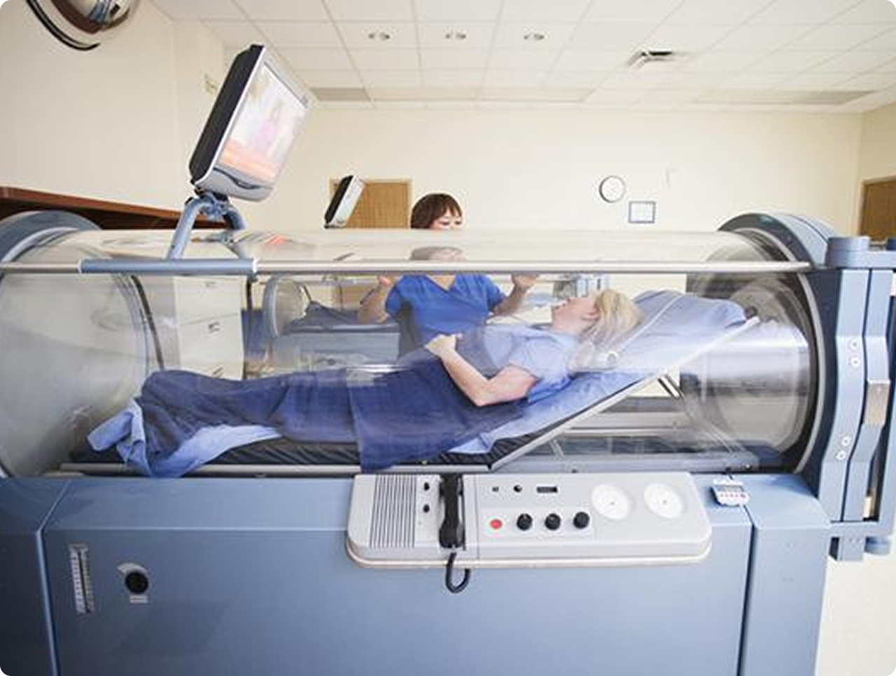 Patient lying inside a medical hyperbaric oxygen chamber with a healthcare worker assisting.