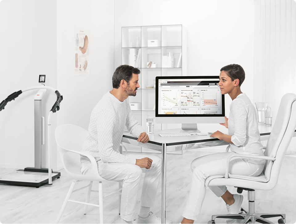 Man and woman discussing data charts displayed on a computer in a bright, modern medical office.