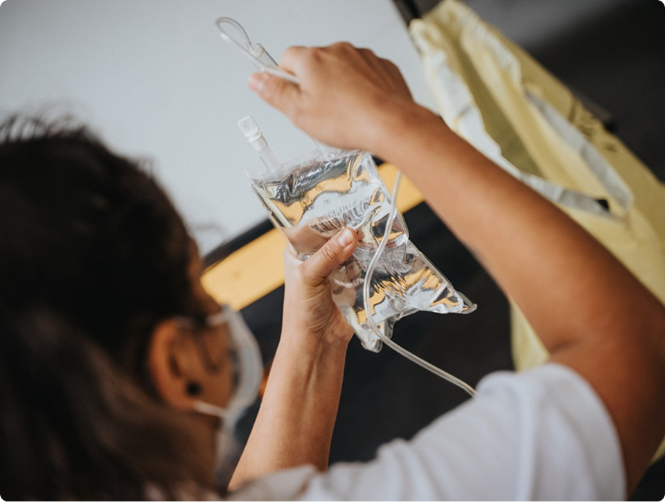 Person wearing a face mask holding and inspecting a clear intravenous fluid bag.