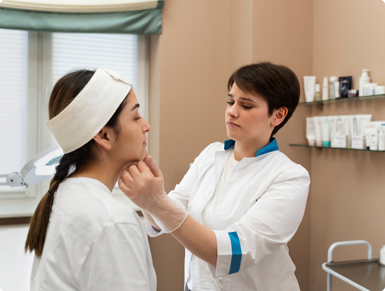 Skincare professional examining a woman's face in a clinic room with skincare products on shelves.