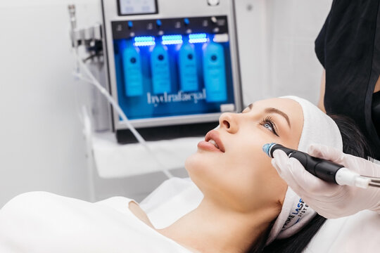 Woman receiving a facial treatment with a handheld skincare device in a clinical setting.