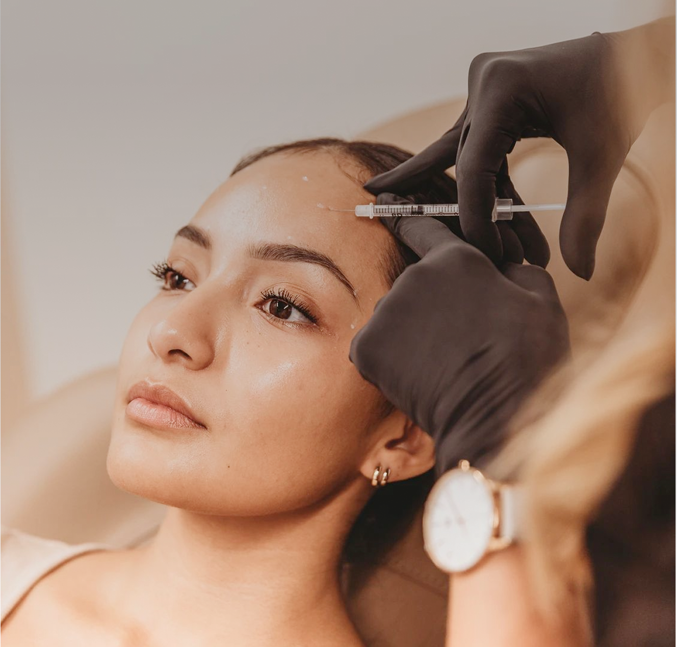 Woman receiving a cosmetic injection on her forehead by a gloved professional.