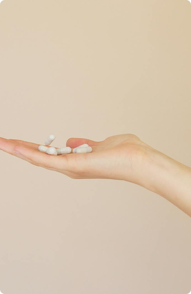 A hand holding several white capsules against a neutral beige background.