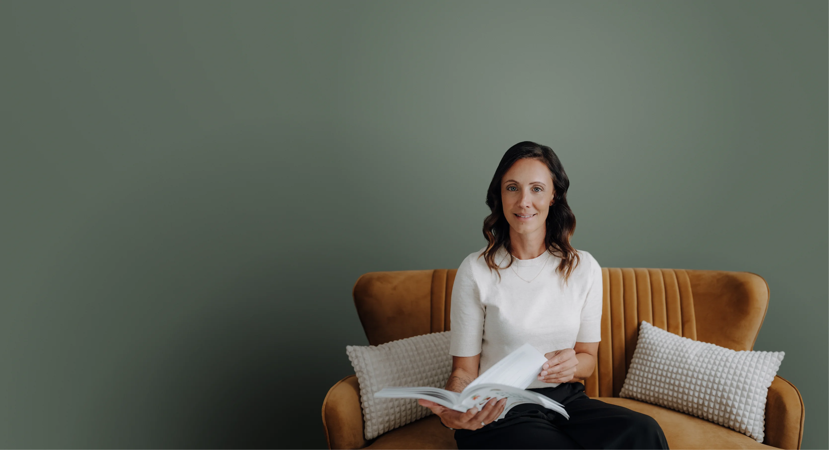 Diätologin Johanna Feichtl sitzt auf einem braunen Sofa und blättert in einem Buch.