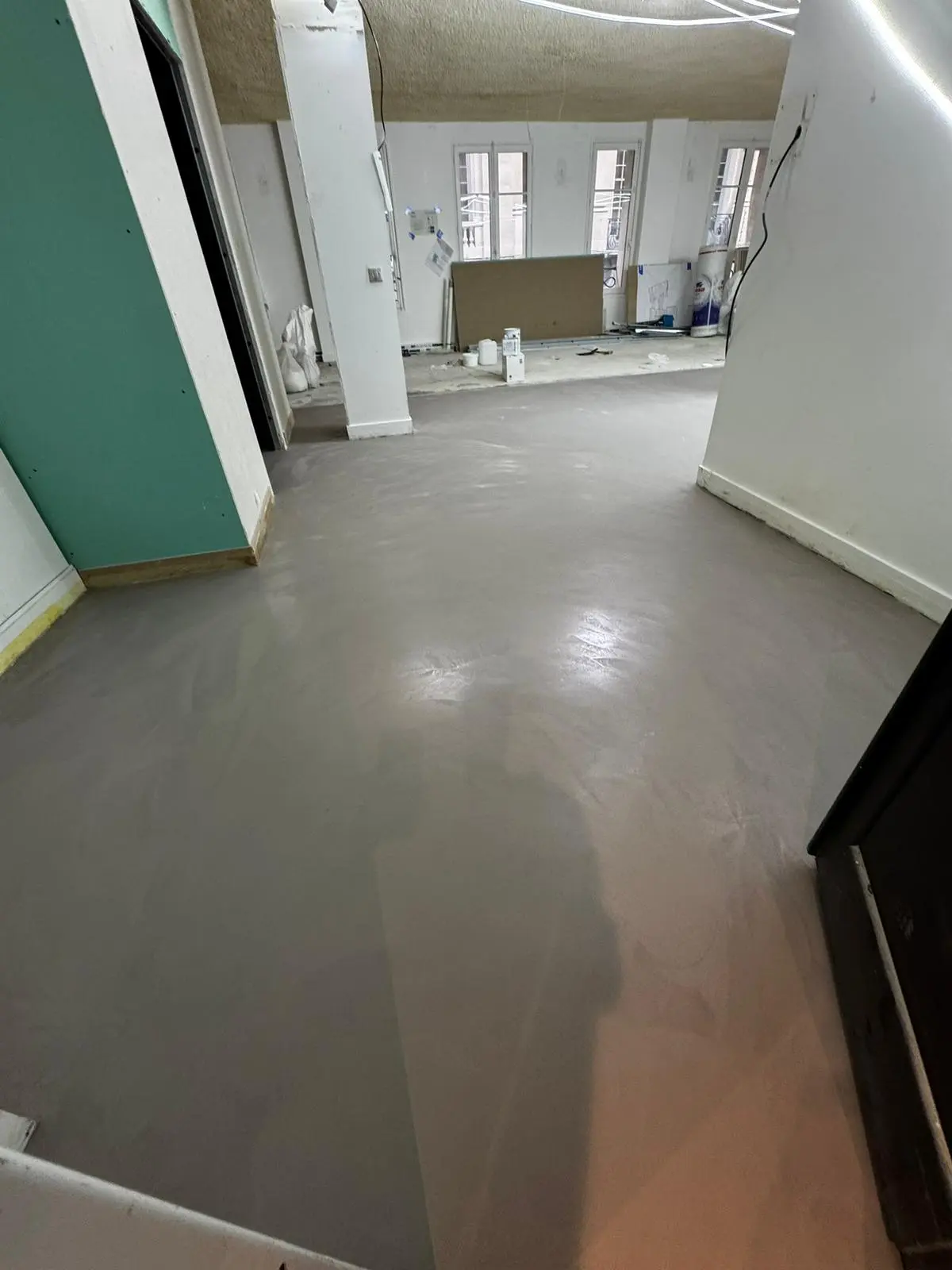 Application d'un béton ciré par un artisan poseur spécialisé au dessus d'un parquet ancien d'un appartement à Paris.