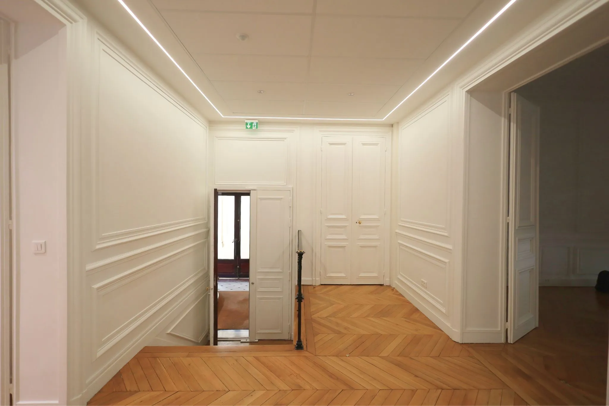 Bureau rénové avec moulures blanches, parquet et éclairage indirect au plafond