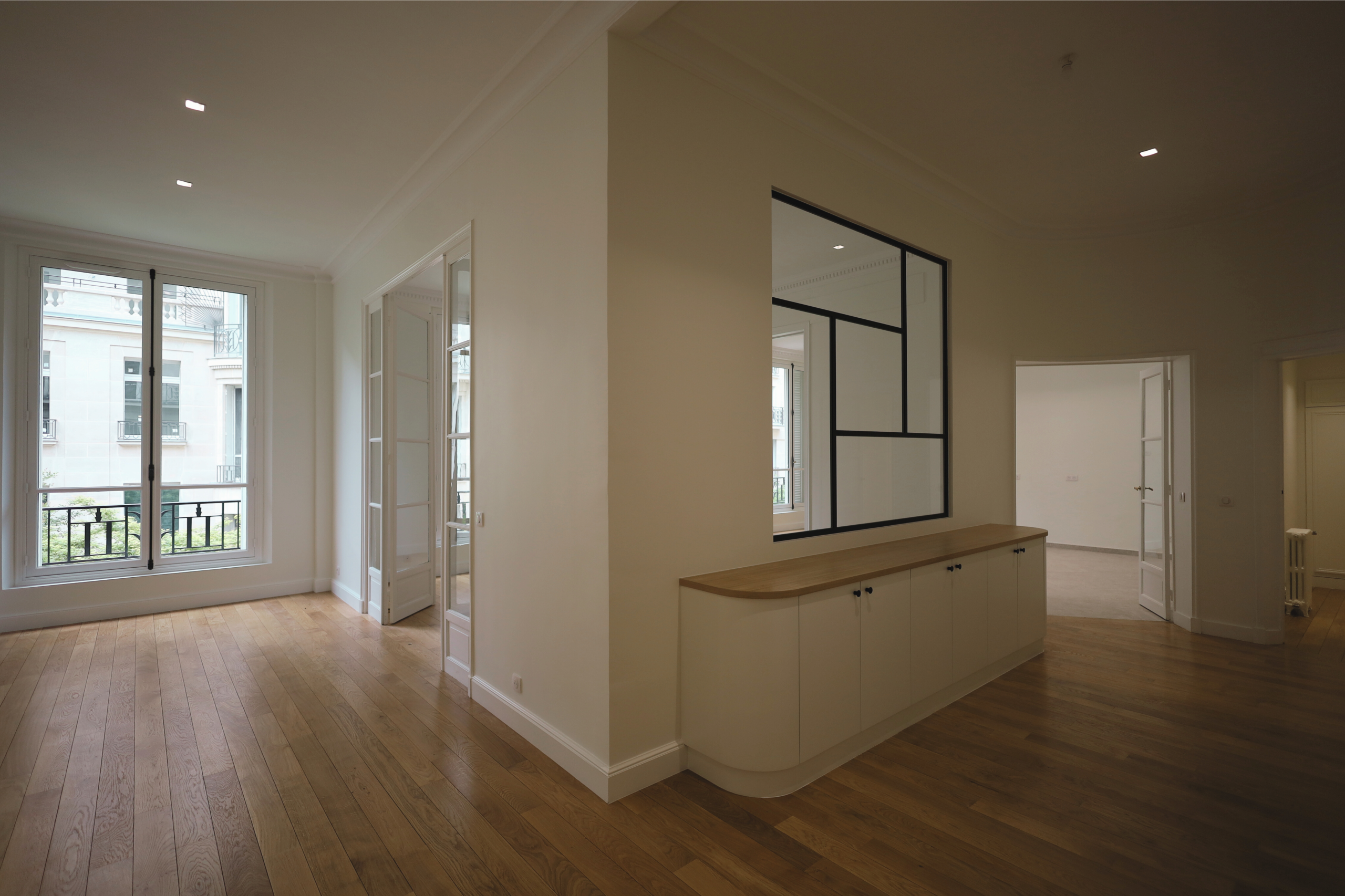 Appartement rénové avec parquet en bois, verrière intérieure noire et grandes fenêtres.