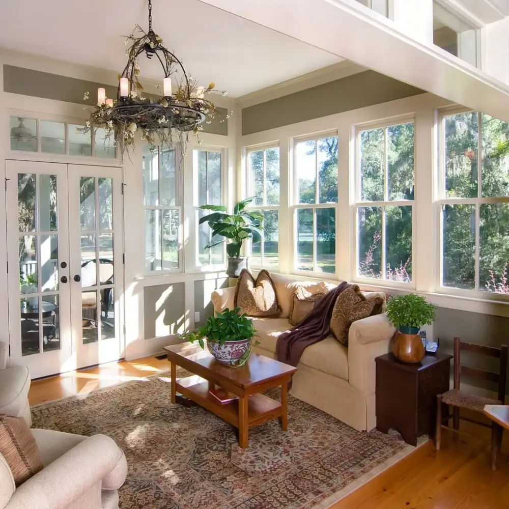 Furnished sunroom with large windows showcasing bright natural light and comfortable seating