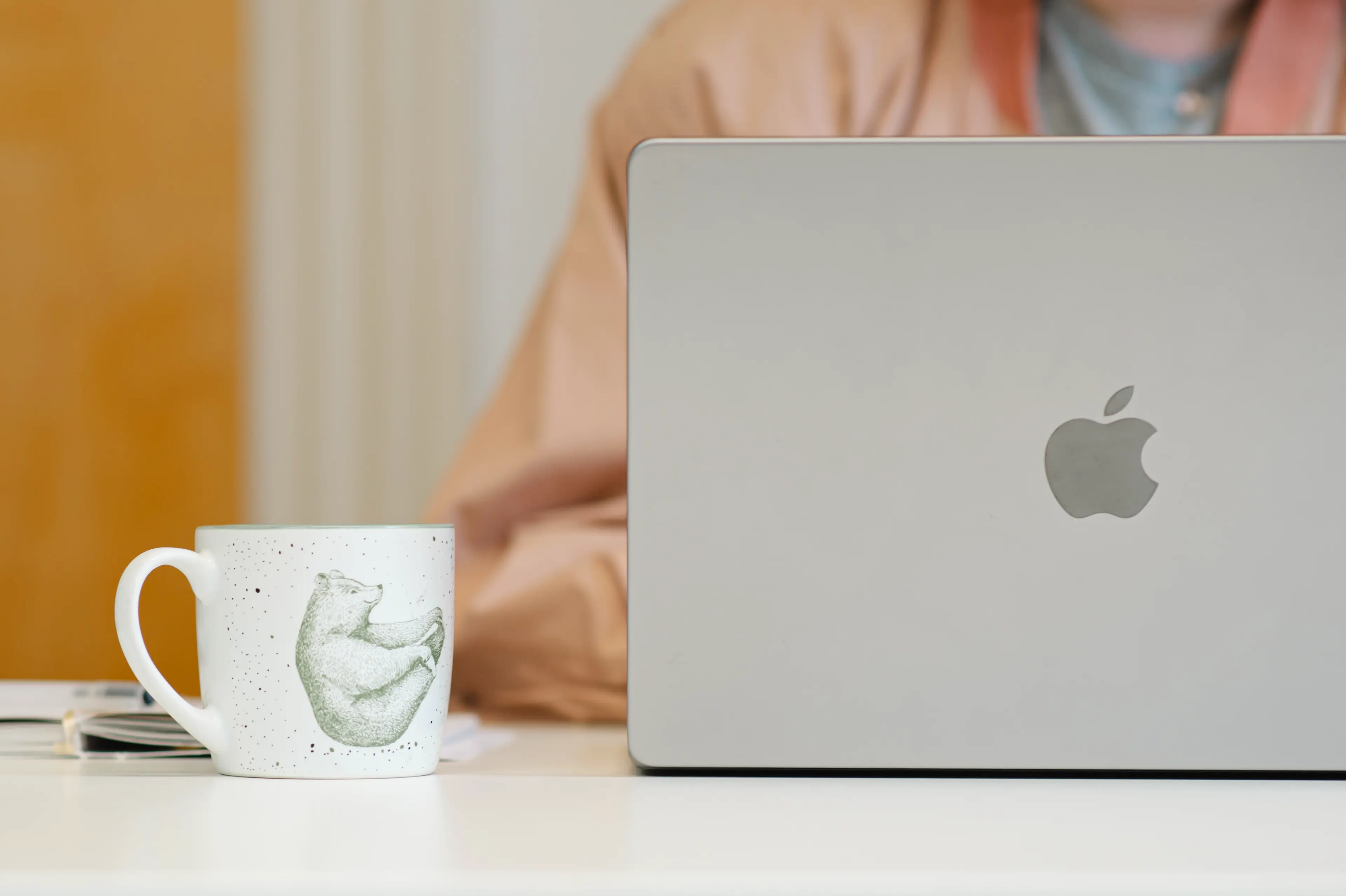 Eine Person arbeitet an einem MacBook. Daneben steht eine Kaffeetasse.