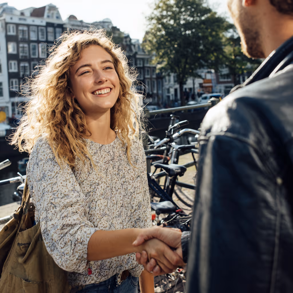 Vrolijke vrouw met krullend haar die handen schudt met een man op straat met fietsen en gebouwen op de achtergrond.