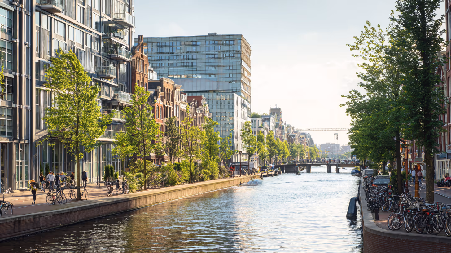 Kanaal in een stad met fietsen en bomen langs de kades en diverse moderne en klassieke gebouwen in de zon.