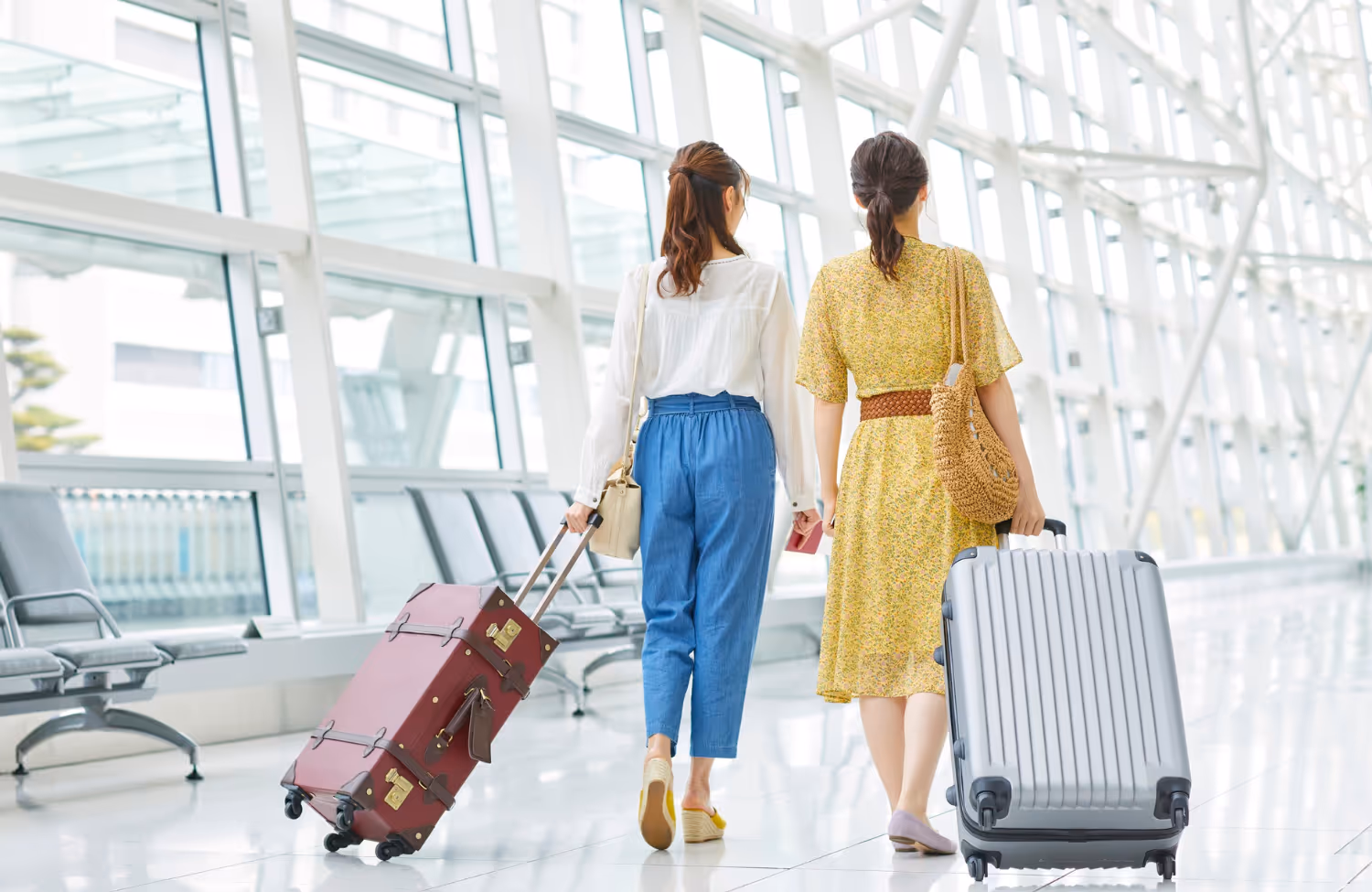 Twee vrouwen met reistassen lopen samen door een lichte, moderne luchthavenhal.