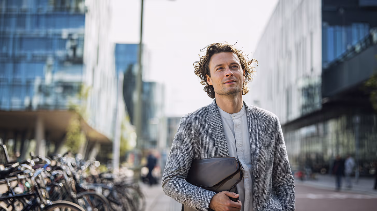 Man met warrig haar en een grijs jasje lopend naast een rij fietsen in een stedelijke omgeving.