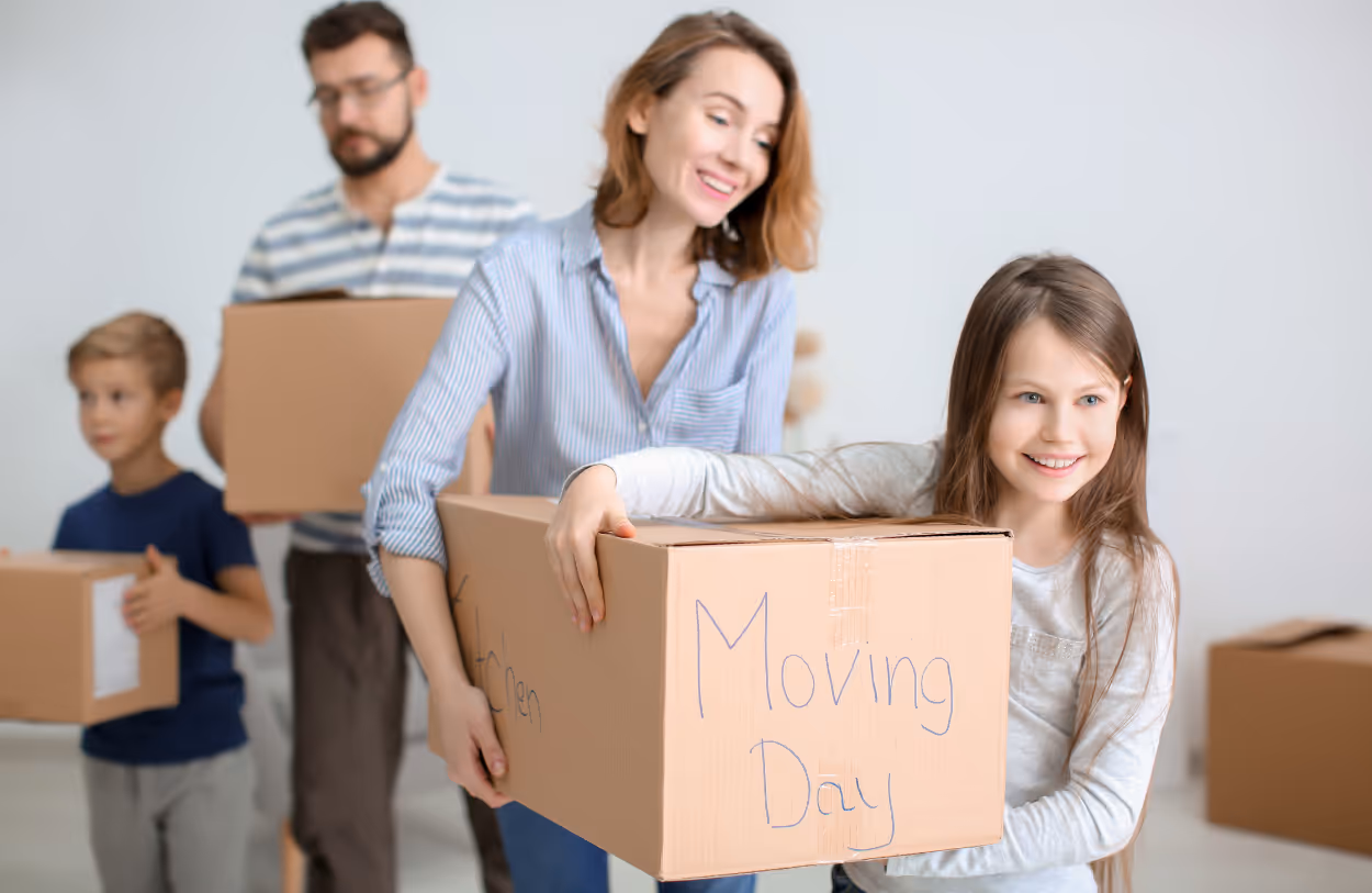 Een gezin met een vrouw, man, jongen en meisje die dozen dragen tijdens verhuizing, waarbij de doos van het meisje ‘Moving Day’ zegt.
