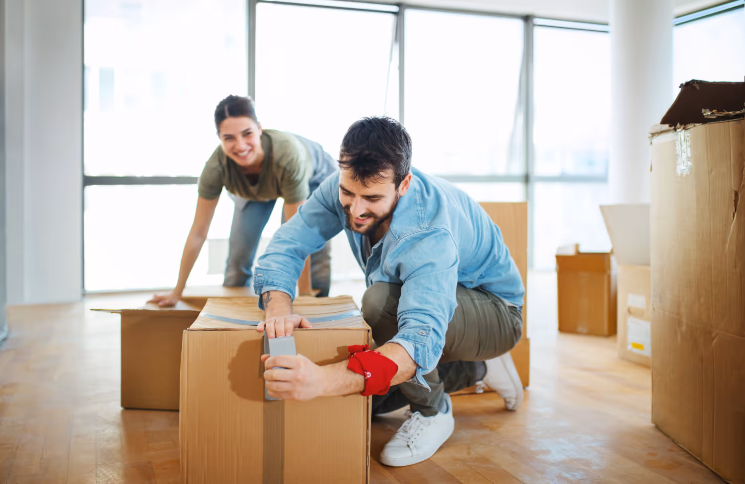 Jong stel dat lachend dozen inpakt in een heldere kamer tijdens het verhuizen.