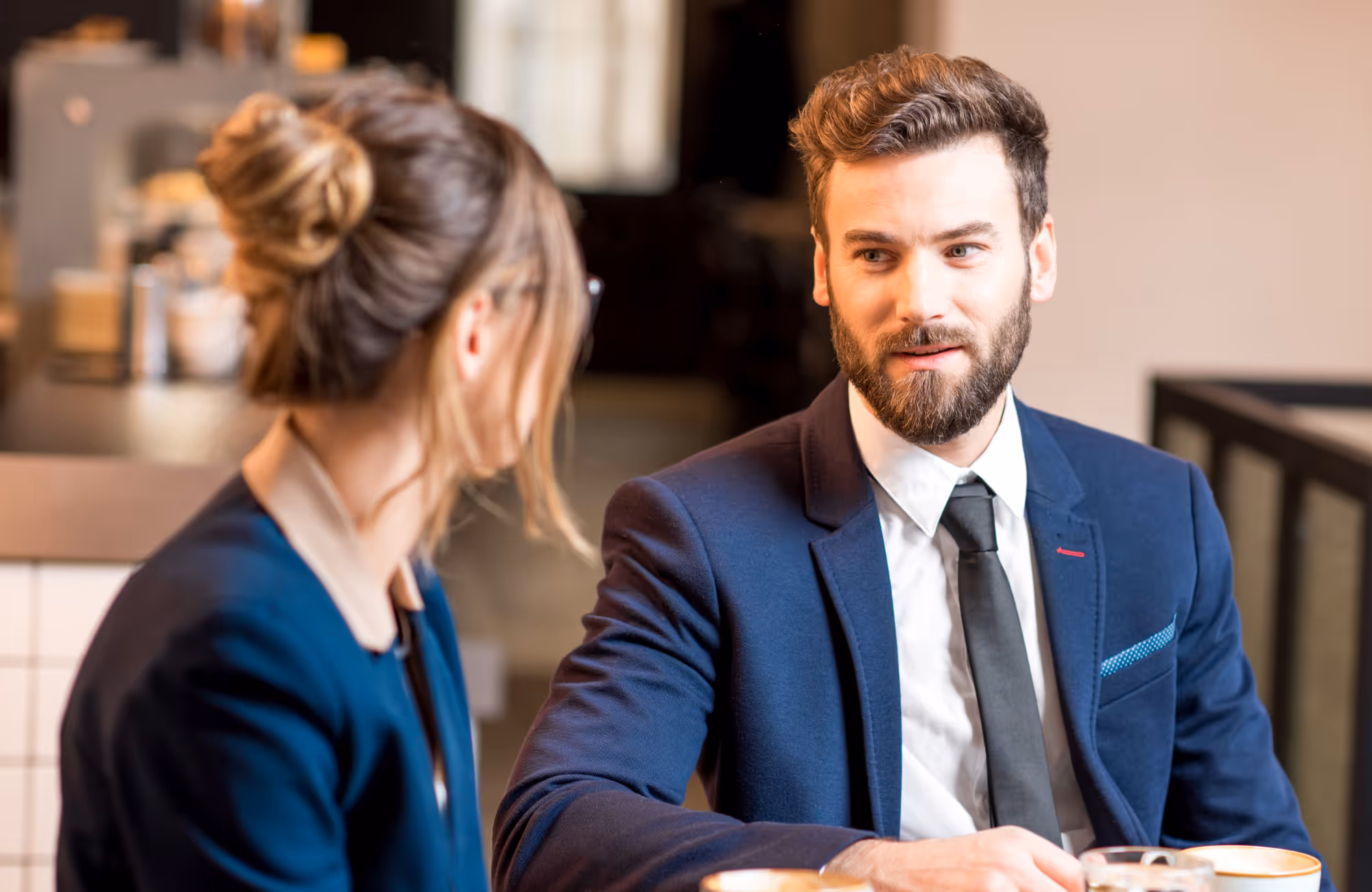 Twee mensen in zakelijke kleding die samen in een café zitten en een gesprek voeren.