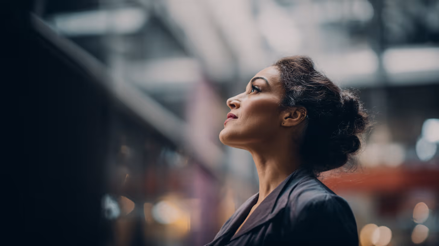 Portret van een vrouw met opgestoken haar die omhoog en naar rechts kijkt in een onscherpe binnenomgeving.