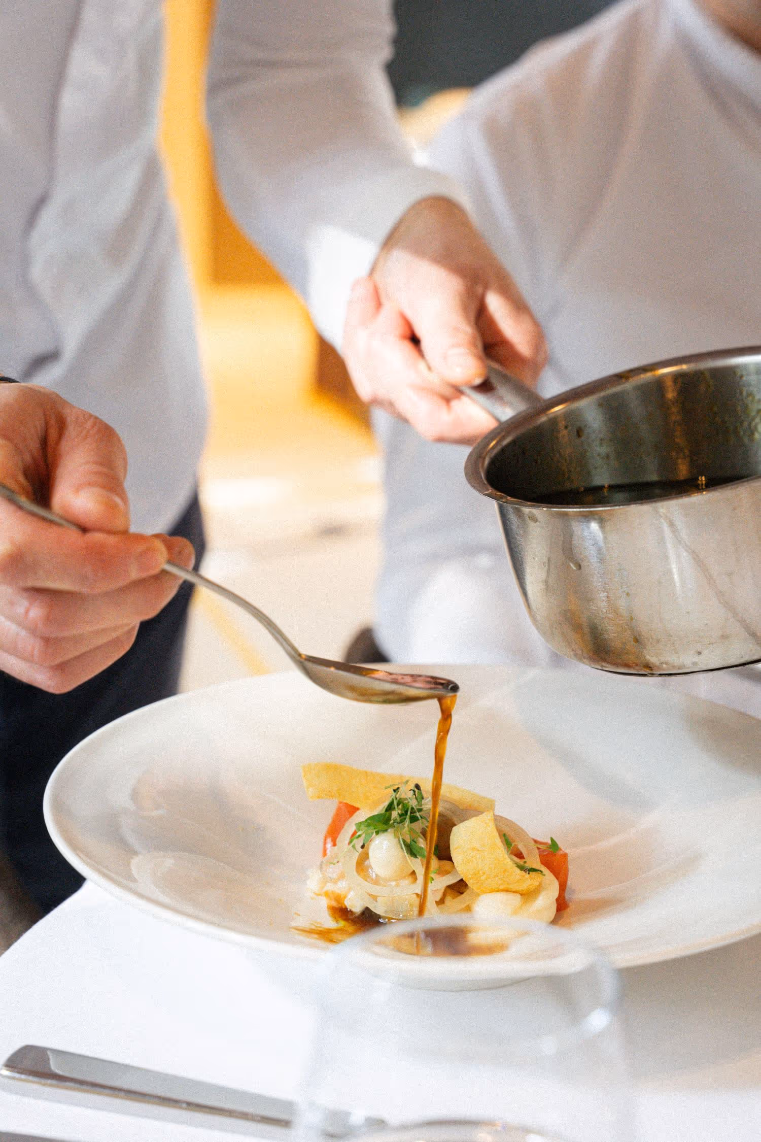 Nahaufnahme einer Vorspeise an welcher gerade aus einem Topf Sauce angegossen wird