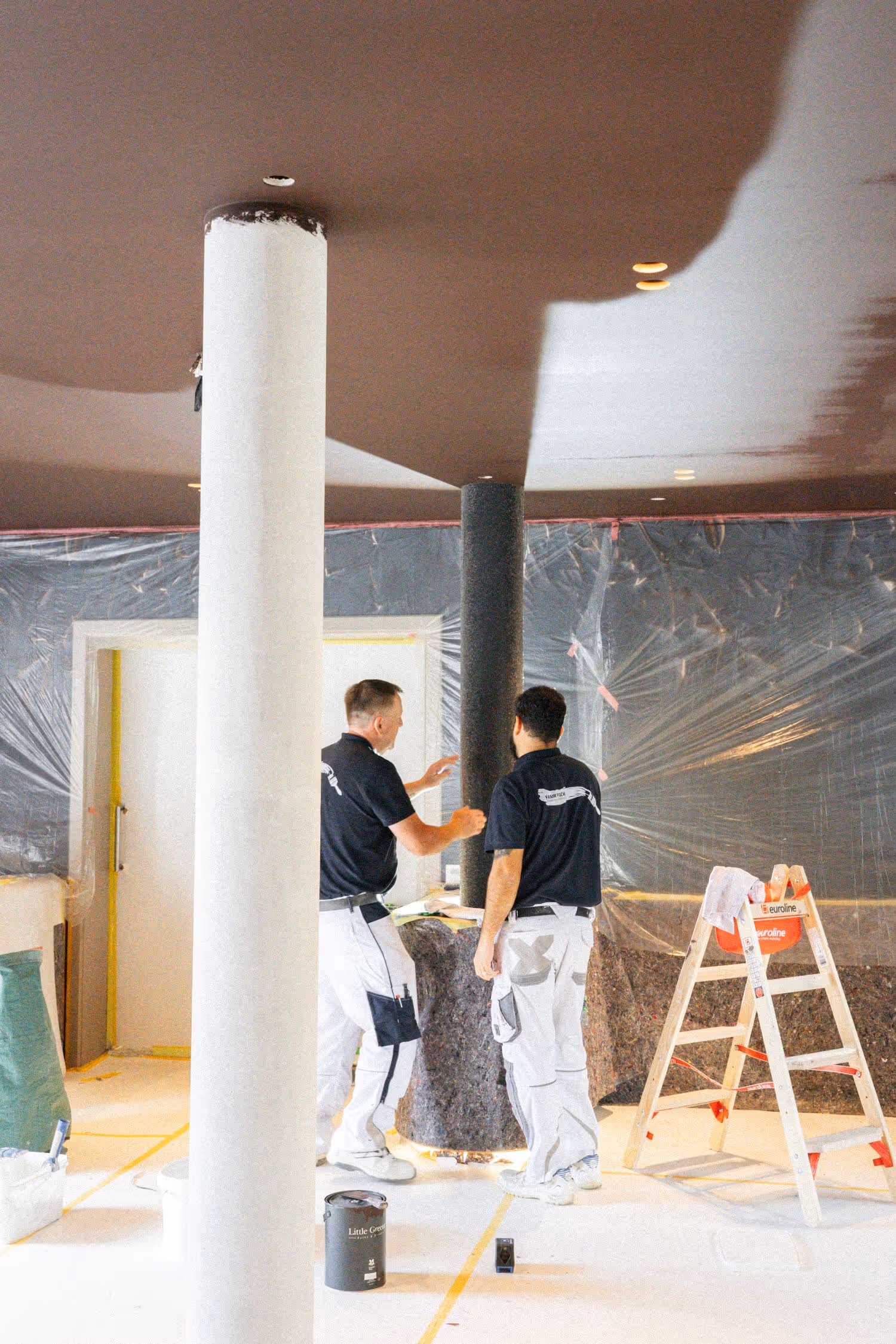 Zwei Handwerker stehen im noch nicht fertiggestellten Restaurant und arbeiten an der Tapete