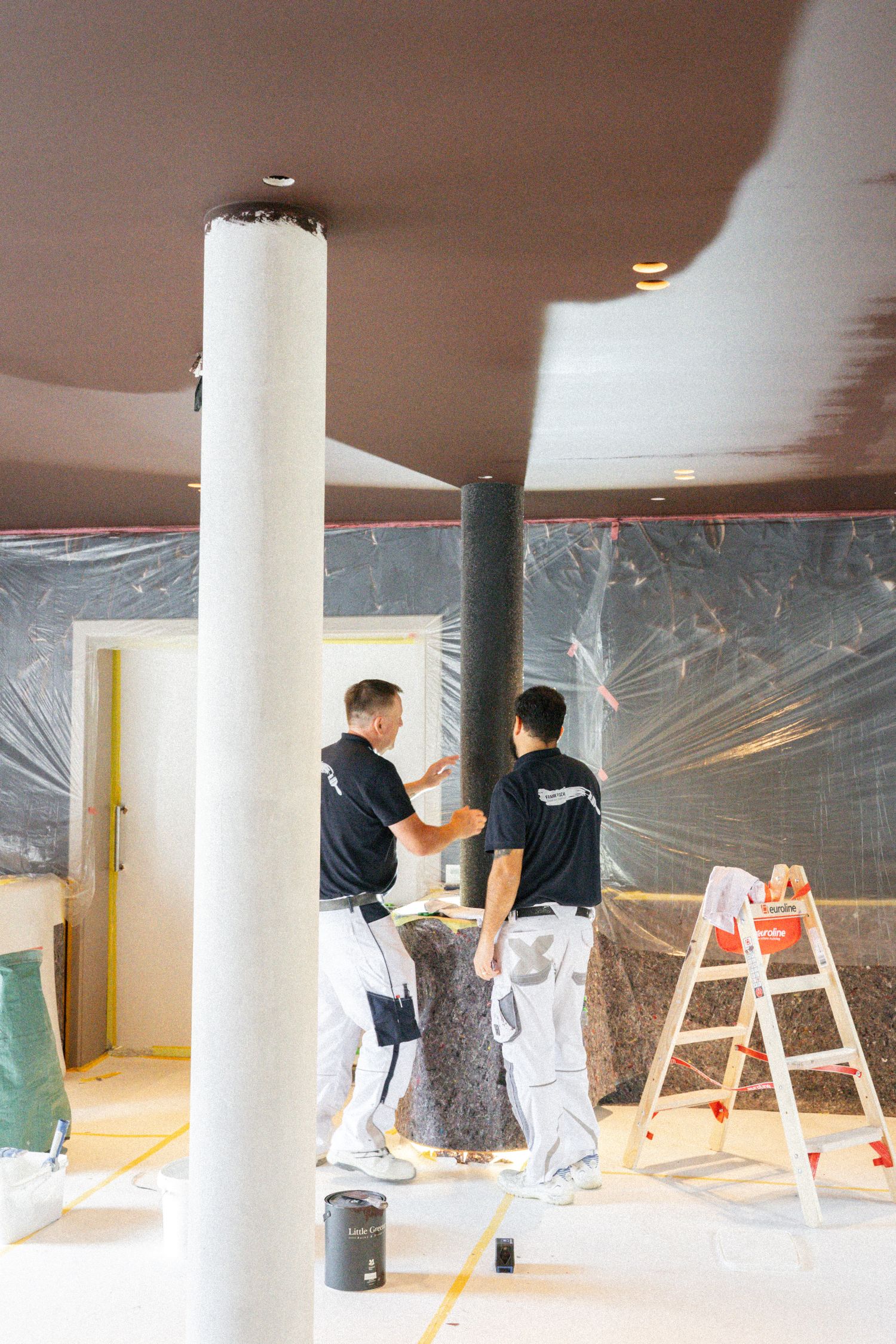 Zwei Handwerker stehen im noch nicht fertiggestellten Restaurant und arbeiten an der Tapete