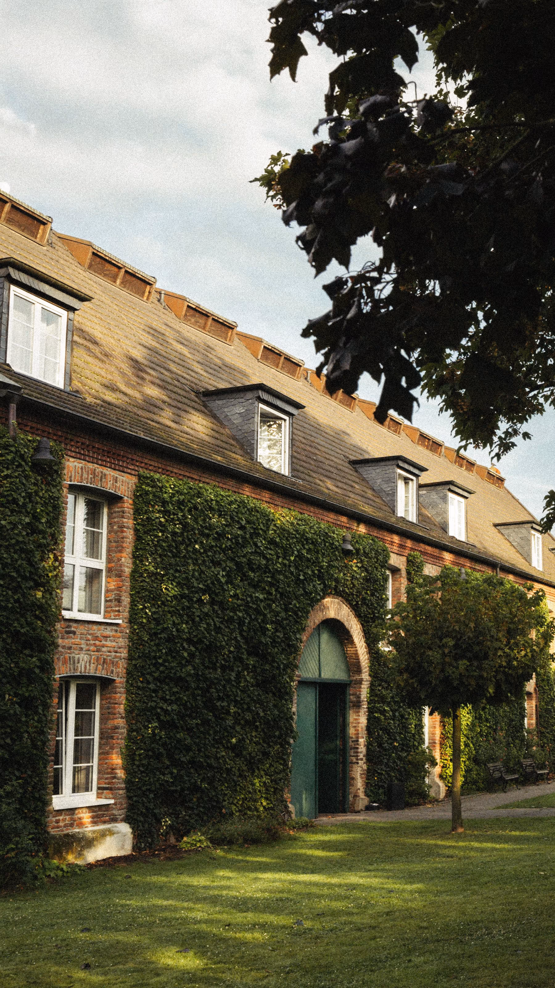 Seitenansicht des Hotel Clostermanns Hof, ein altes Steingebäude mit Efeu und grüner Wiese