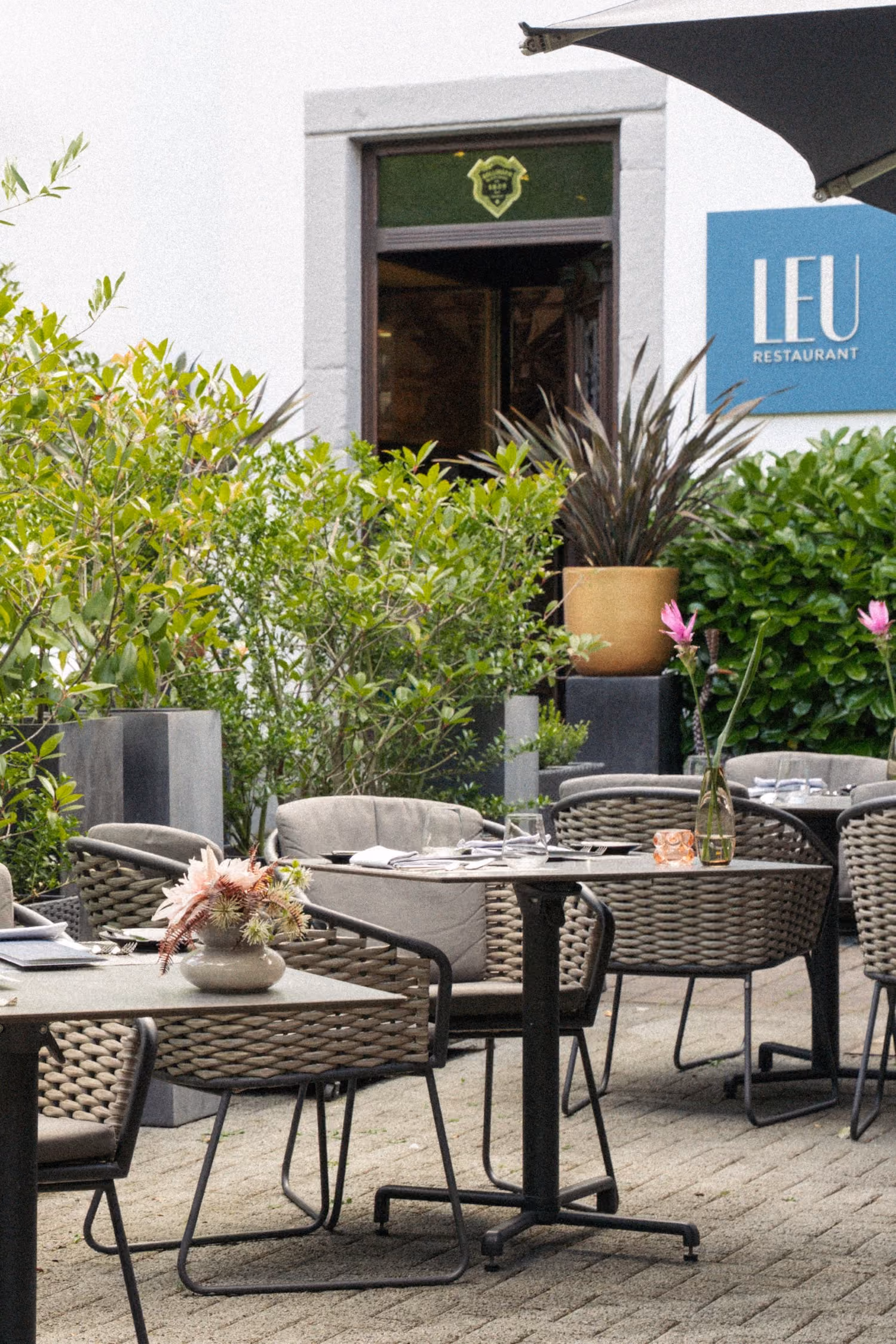 Mehrere eingedeckte Tische auf der Terrasse des Restaurants mit Sträuchern umsäumt