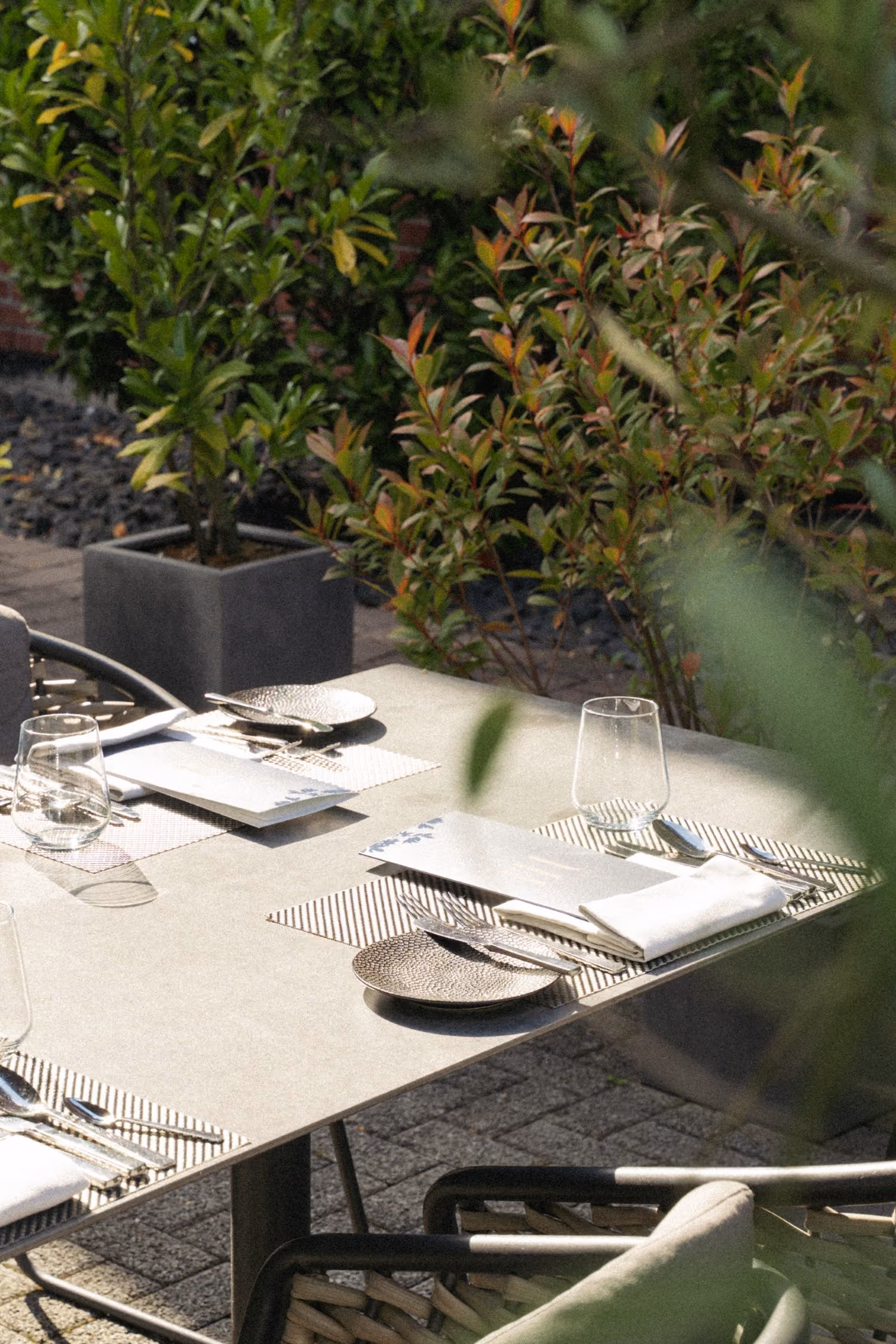 Mehrere eingedeckte Tische auf der Terrasse des Restaurants mit Sträuchern umsäumt