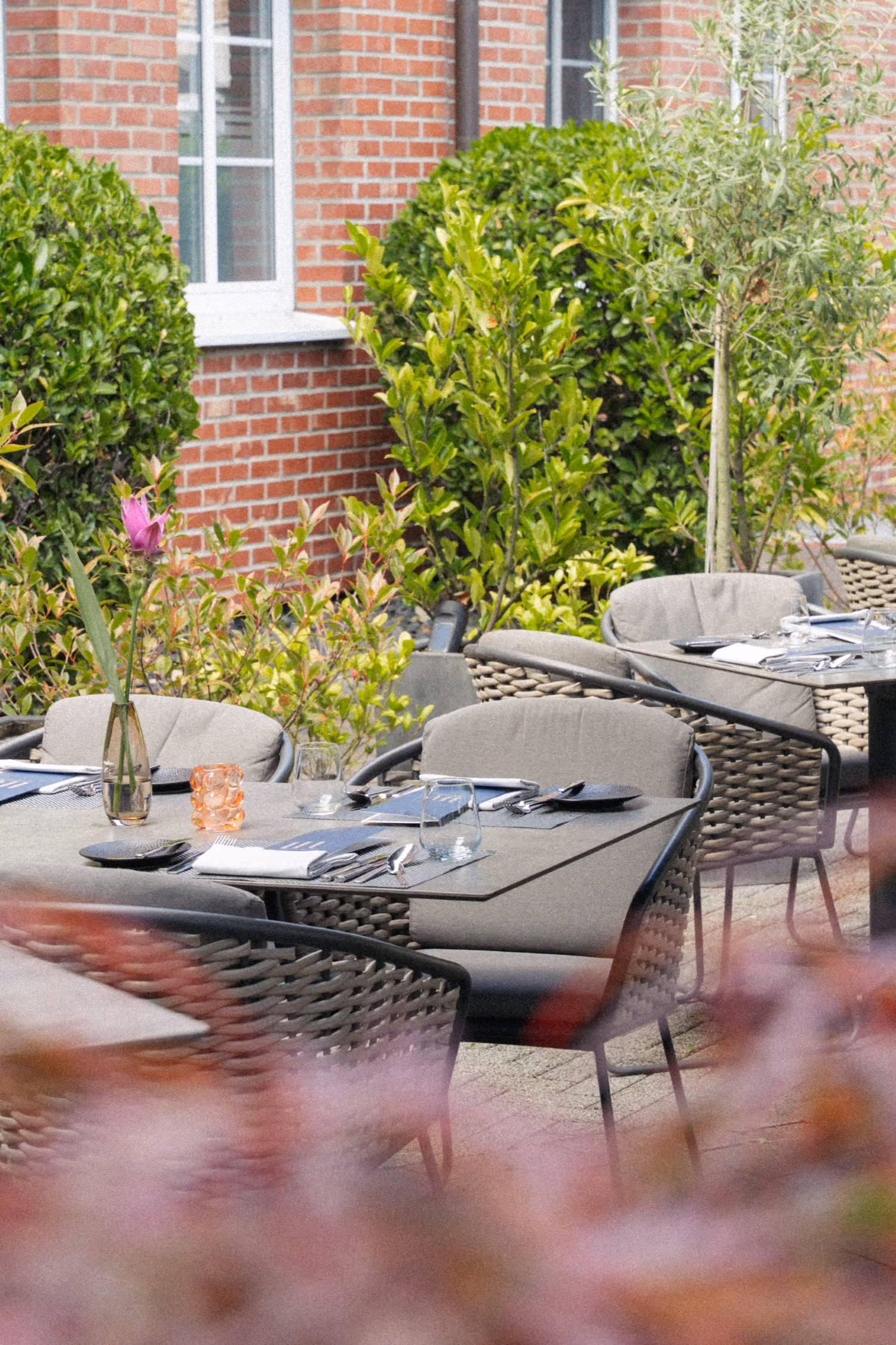 Mehrere eingedeckte Tische auf der Terrasse des Restaurants mit Sträuchern umsäumt