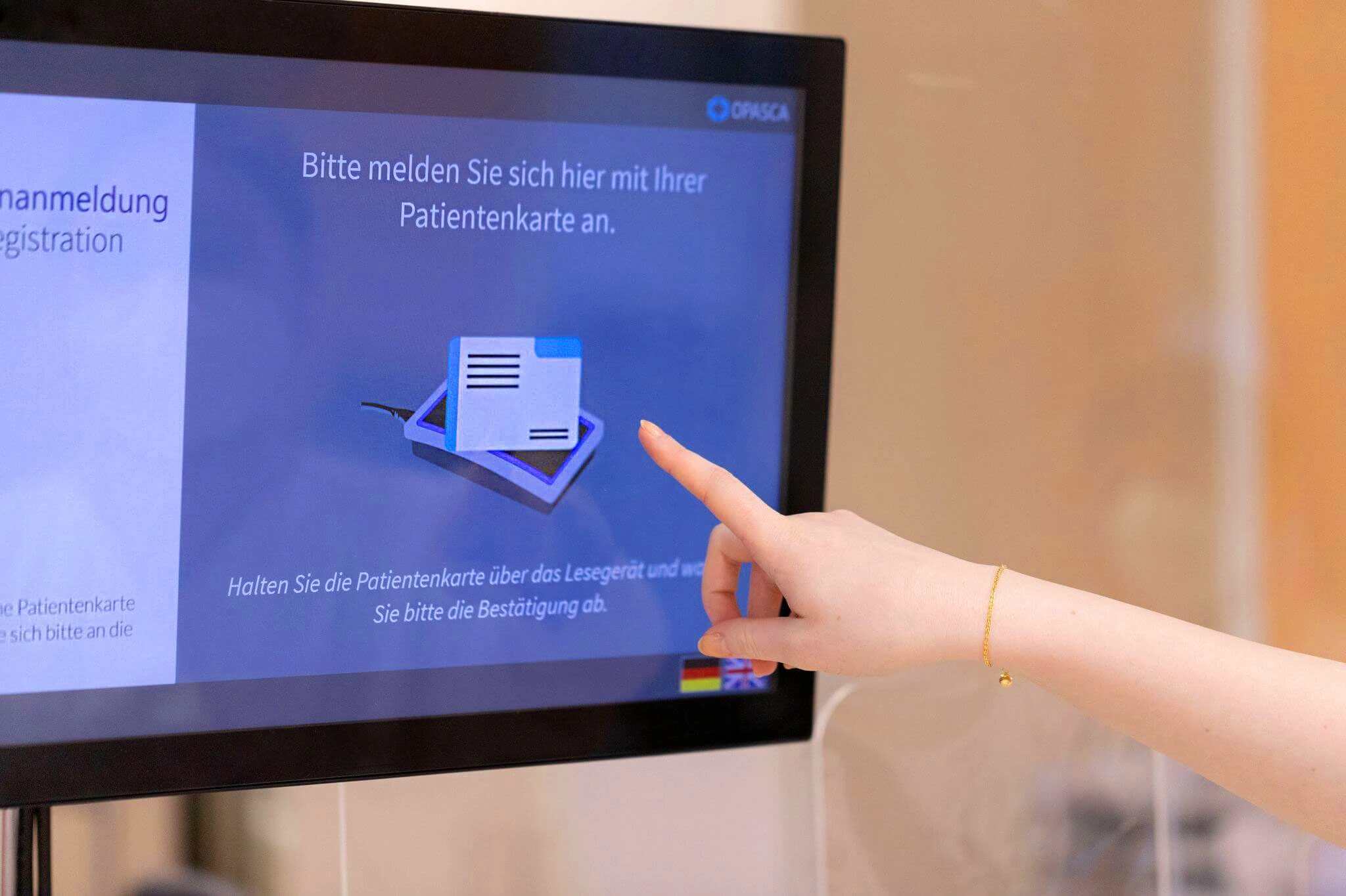 Hand zeigt auf Bildschirm mit Anweisung, sich mit Patientekarte anzumelden.