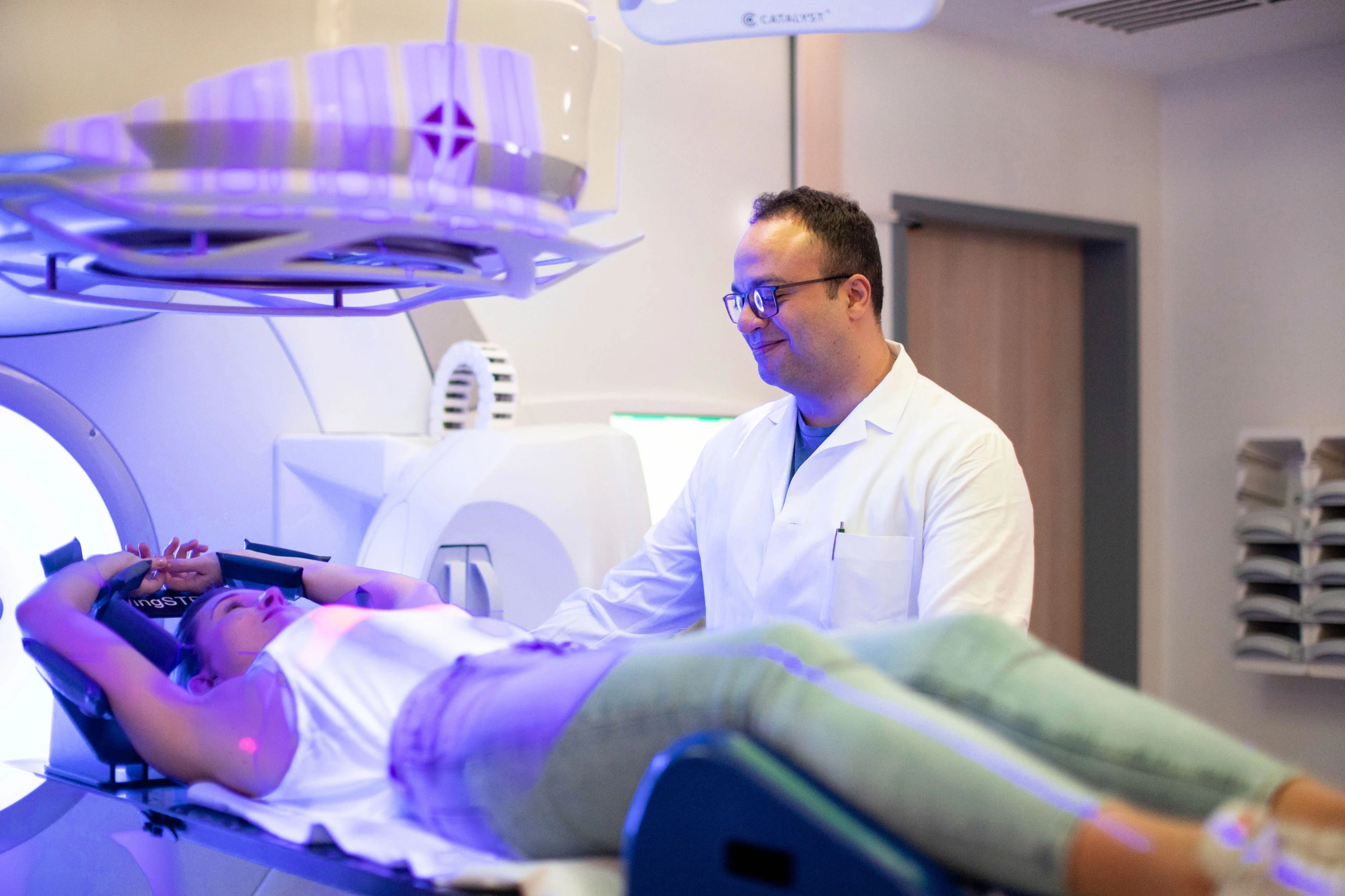 Arzt im weißen Kittel betreut Patientin, die in einer medizinischen Röntgenanlage liegt.
