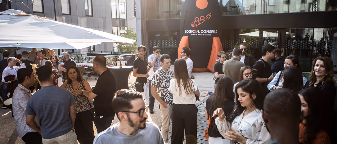 Un groupe de personnes discute lors d'un événement en plein air avec un grand ballon gonflable marqué « Logic@l Conseils » en arrière-plan.