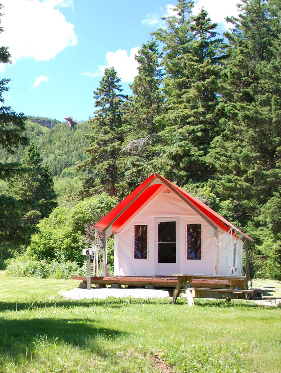 Une tente prête à camper dans la forêt de Percé avec en arrière-plan la plateforme suspendue vitrée